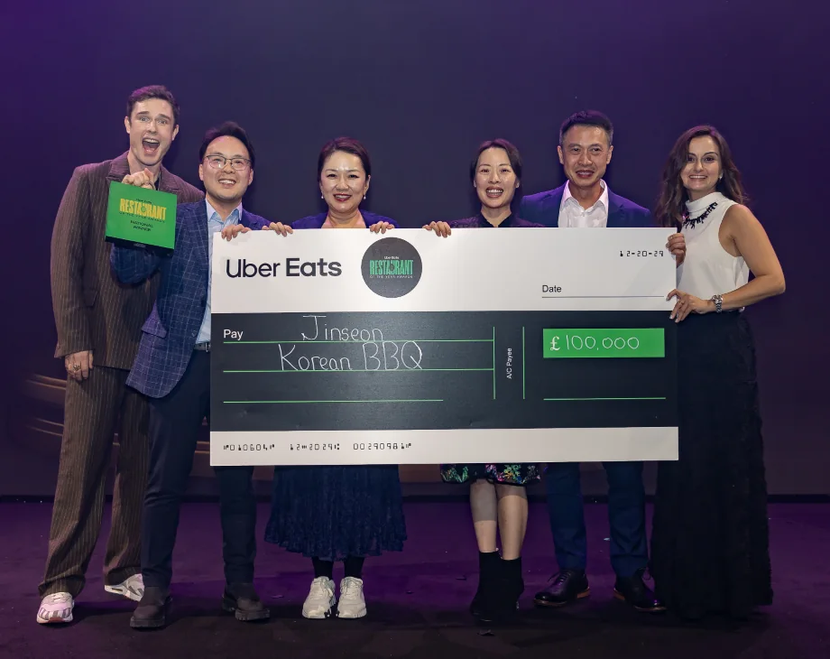 The Jinseon family on stage at the Uber Eats Restaurant of the Year awards with host Ed Gamble, holding a giant £100,000 cheque made out to Jinseon Korean BBQ.