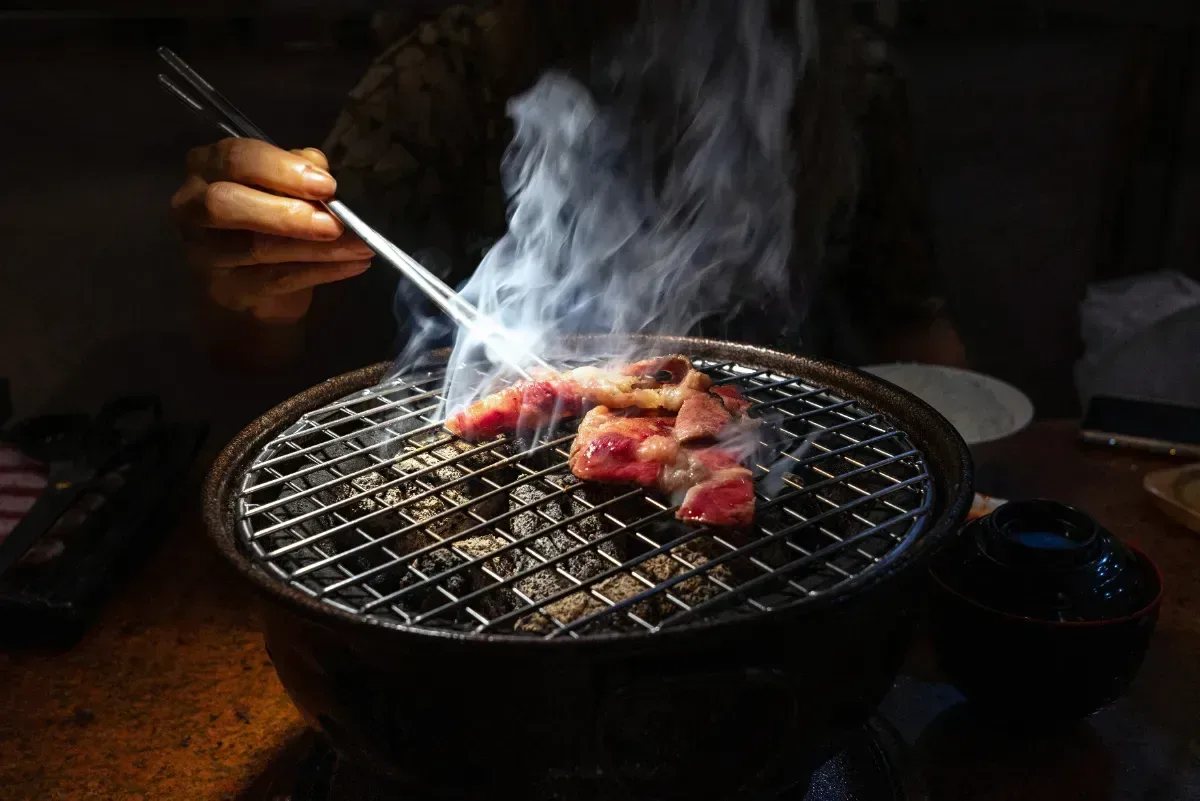 A charcoal grill set into the table, meat searing on the wire grate with smoke rising
